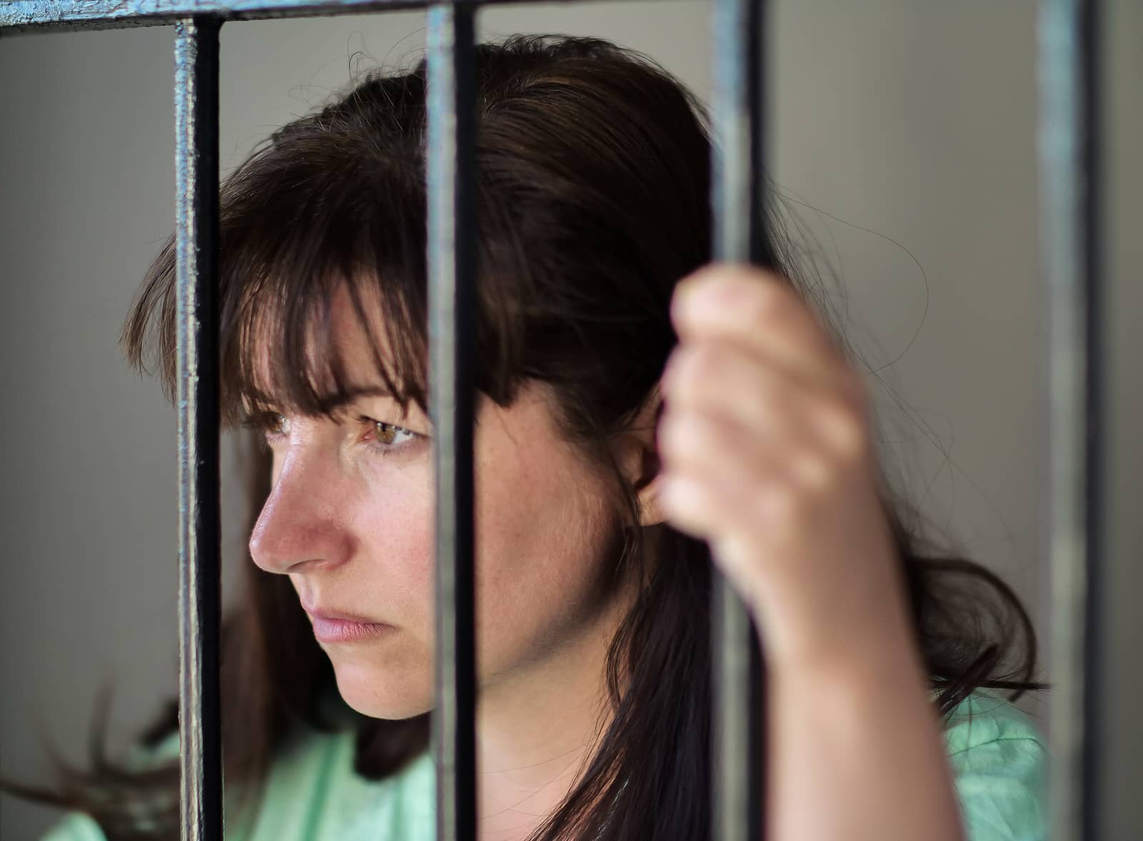 The girl is imprisoned in jail, behind bars.