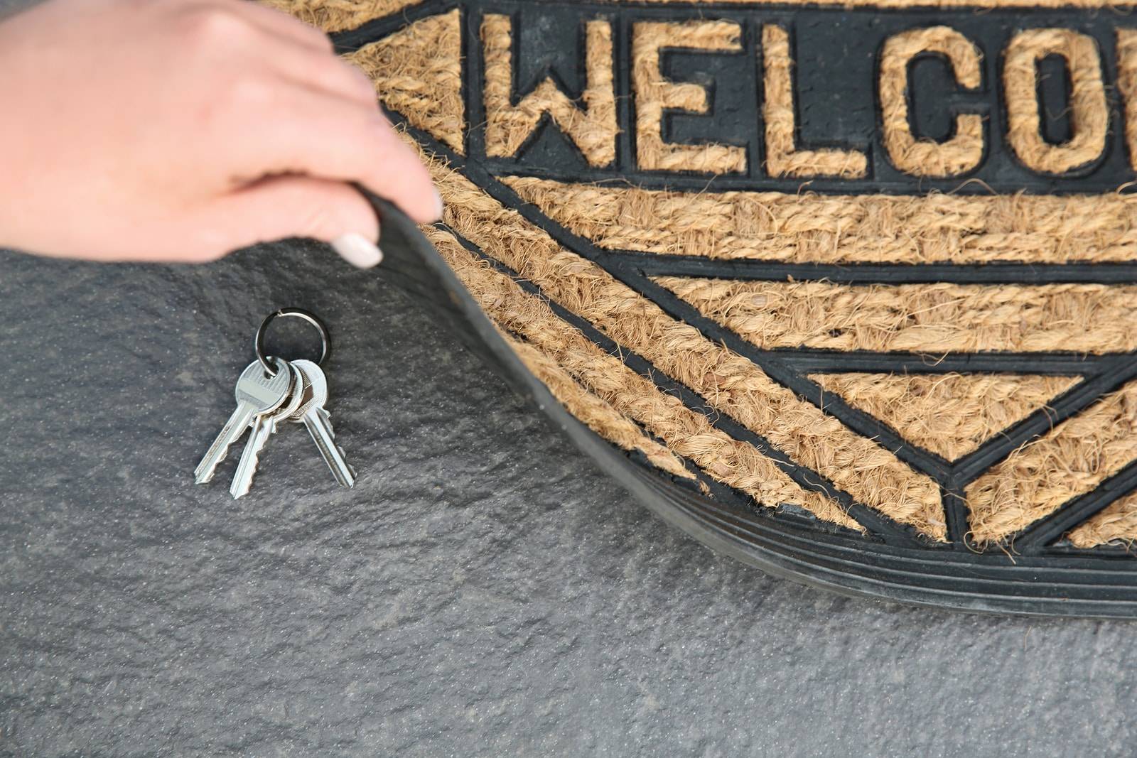 Young woman revealing hidden key under door mat,