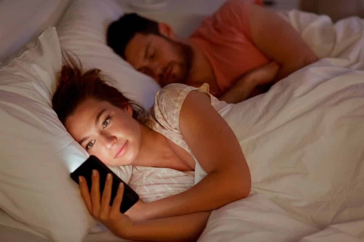 woman using smartphone at night while her boyfriend is sleeping