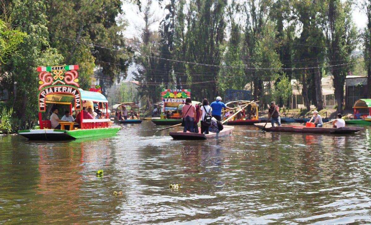 Several colored boats with tourists and gondoliers at exotic Floating Gardens in Mexican city with clear blue sky in warm sunny winter day