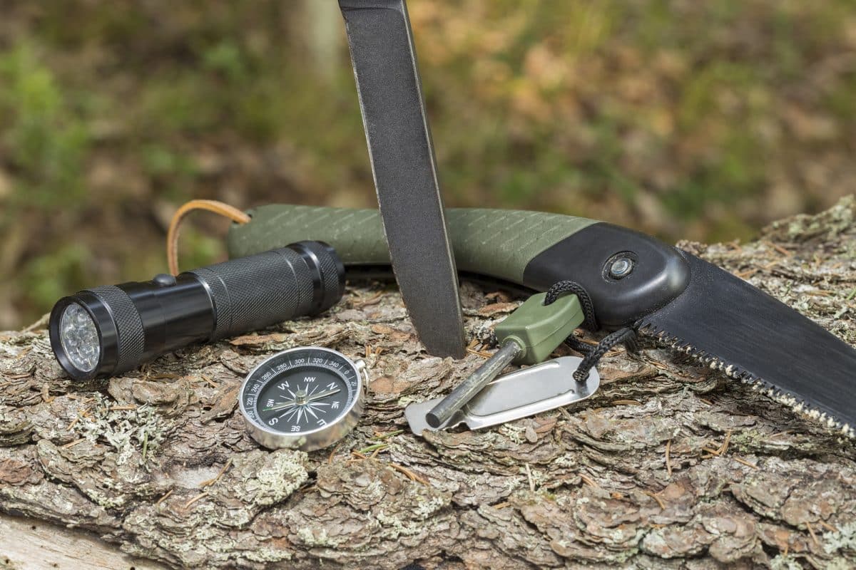 Knife, flashlight, compass, flint and saw on the stump in the forest.