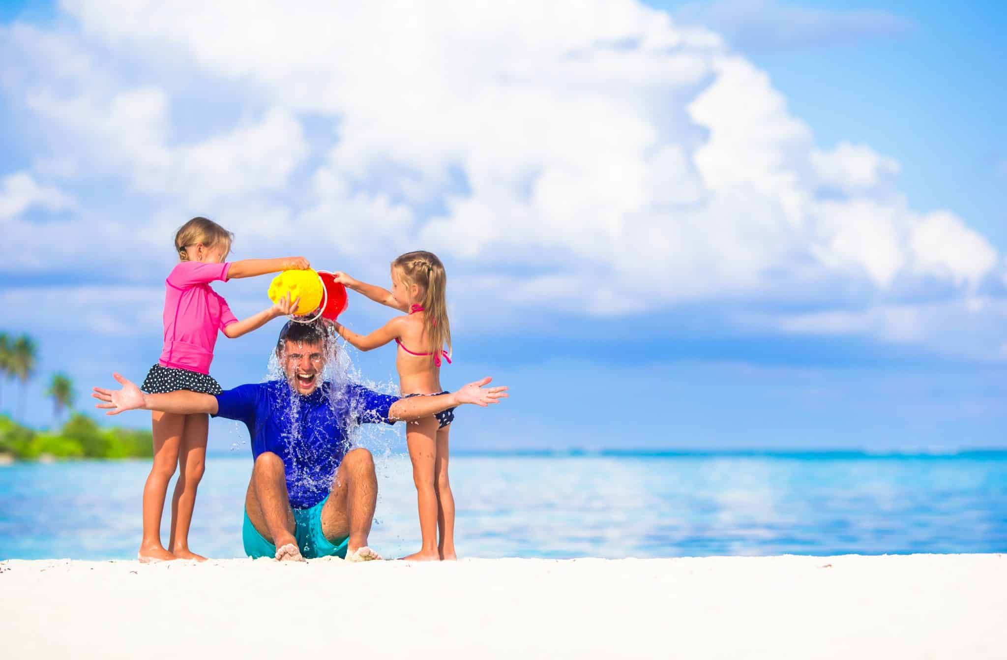 Father and two girls playing with sand on tropical beach, Children That Take Vacations are Smarter