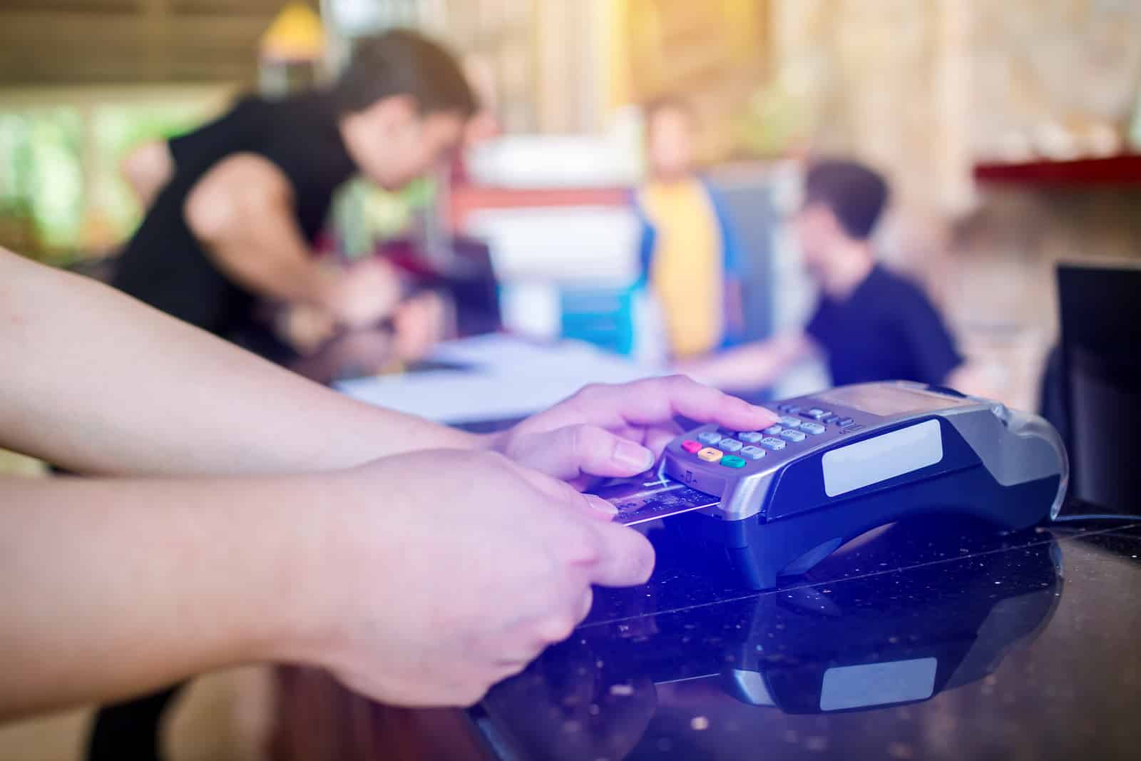 Hand put credit card In slot of credit card reader with blurry cashier