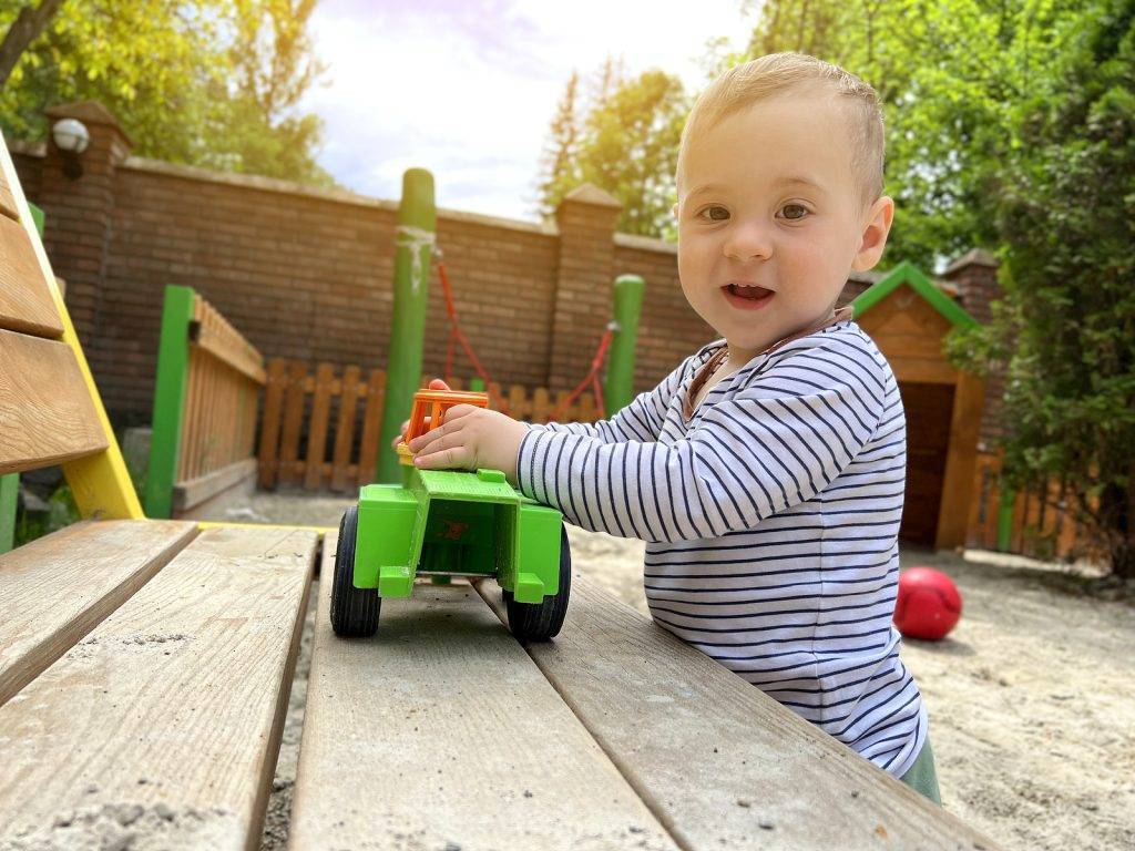 A little cute boy of one and a half years plays with toy car at the playground. Adorable toddler playing with cars and toys outdoor. Family, holiday, kids lifestyle concept. Selective focus